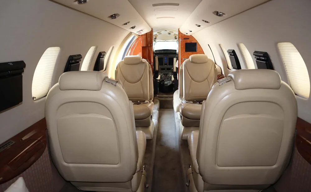 The interior cabin of a business jet with beige leather seats, looking forward towards the cockpit.