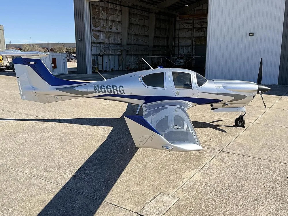 A silver and blue Diamond DA40 aircraft, N66RG, parked on an airfield tarmac in front of a hangar.