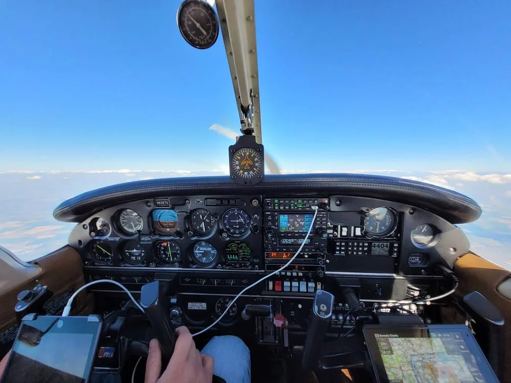 The cockpit of a Piper Archer II in flight, showing the instrument panel and controls with a clear blue sky outside.