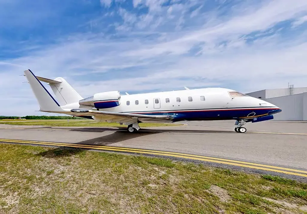 A white business jet with blue and red stripes on the fuselage and tail, parked on an airfield.