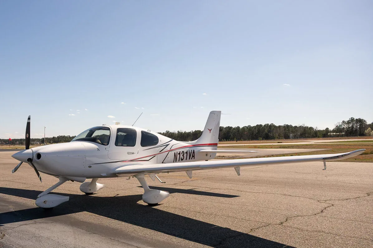 A white Cirrus SR22 aircraft with red and black accent stripes, tail number N131VA, parked on an airfield.