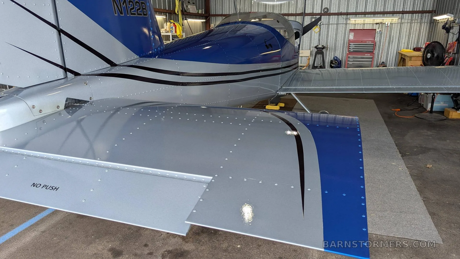 The tail and wing of a blue and silver aircraft, with registration N122B, inside a hangar.