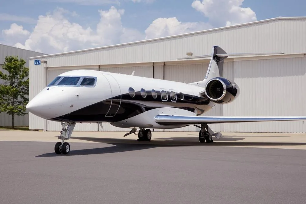 A white and black Gulfstream G600/G650 business jet parked on an airfield in front of a hangar.