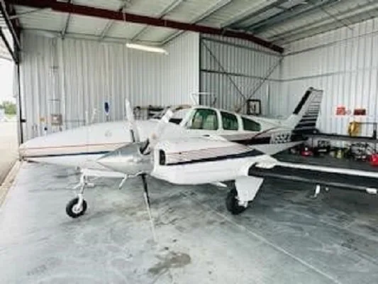 A white and blue twin-engine aircraft, N55EZ, is parked inside a hangar, viewed from the front-left.