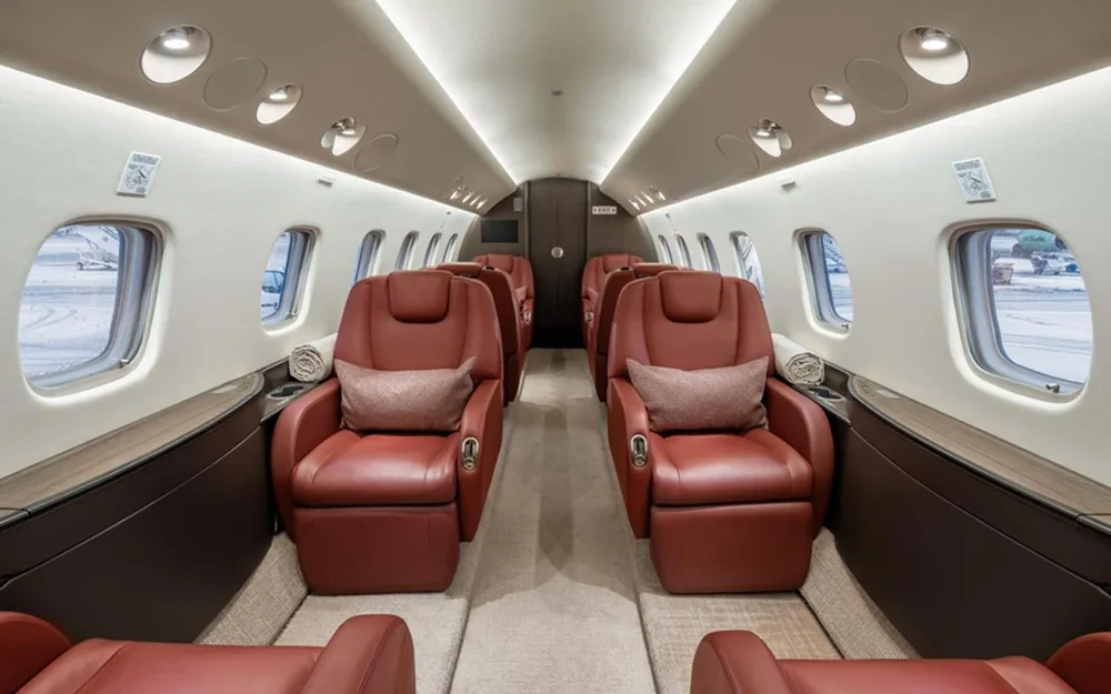 A wide view of a private jet cabin featuring two rows of plush red leather seats facing each other.