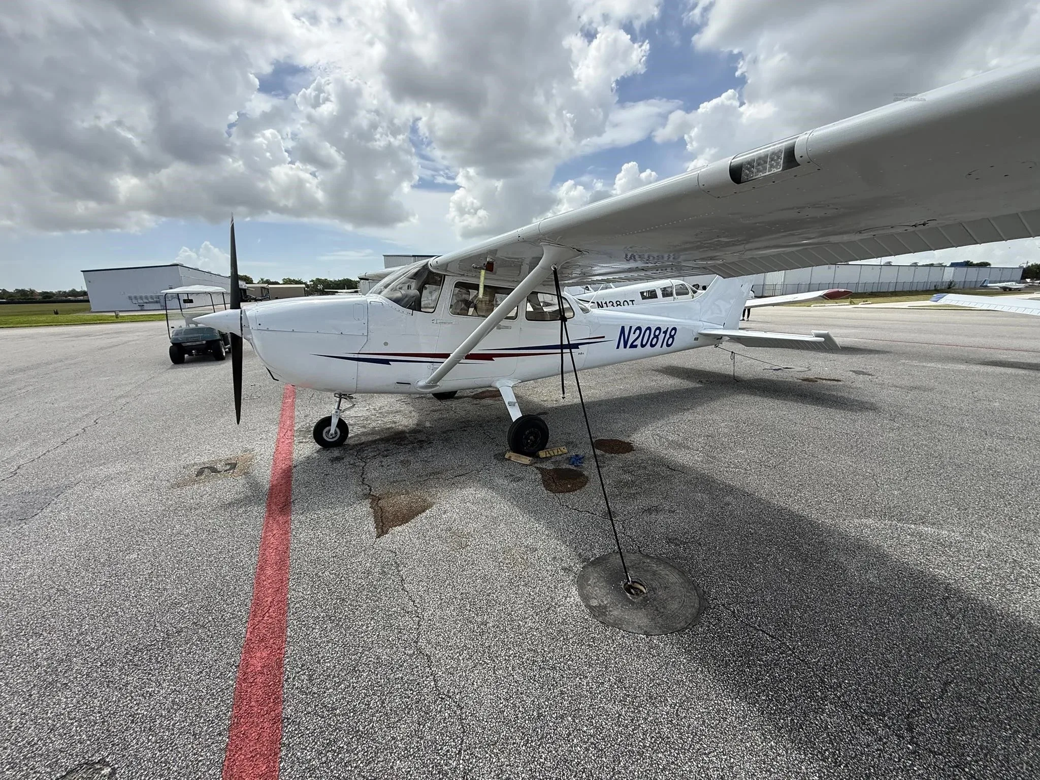 A white Cessna 172 (N20818) parked on an airport tarmac, viewed from the front-right.