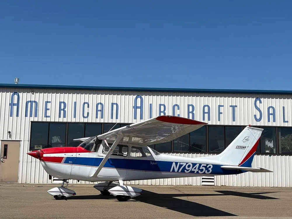 A white, red, and blue Cessna Skyhawk N79453 parked on an tarmac with a hangar in the background.