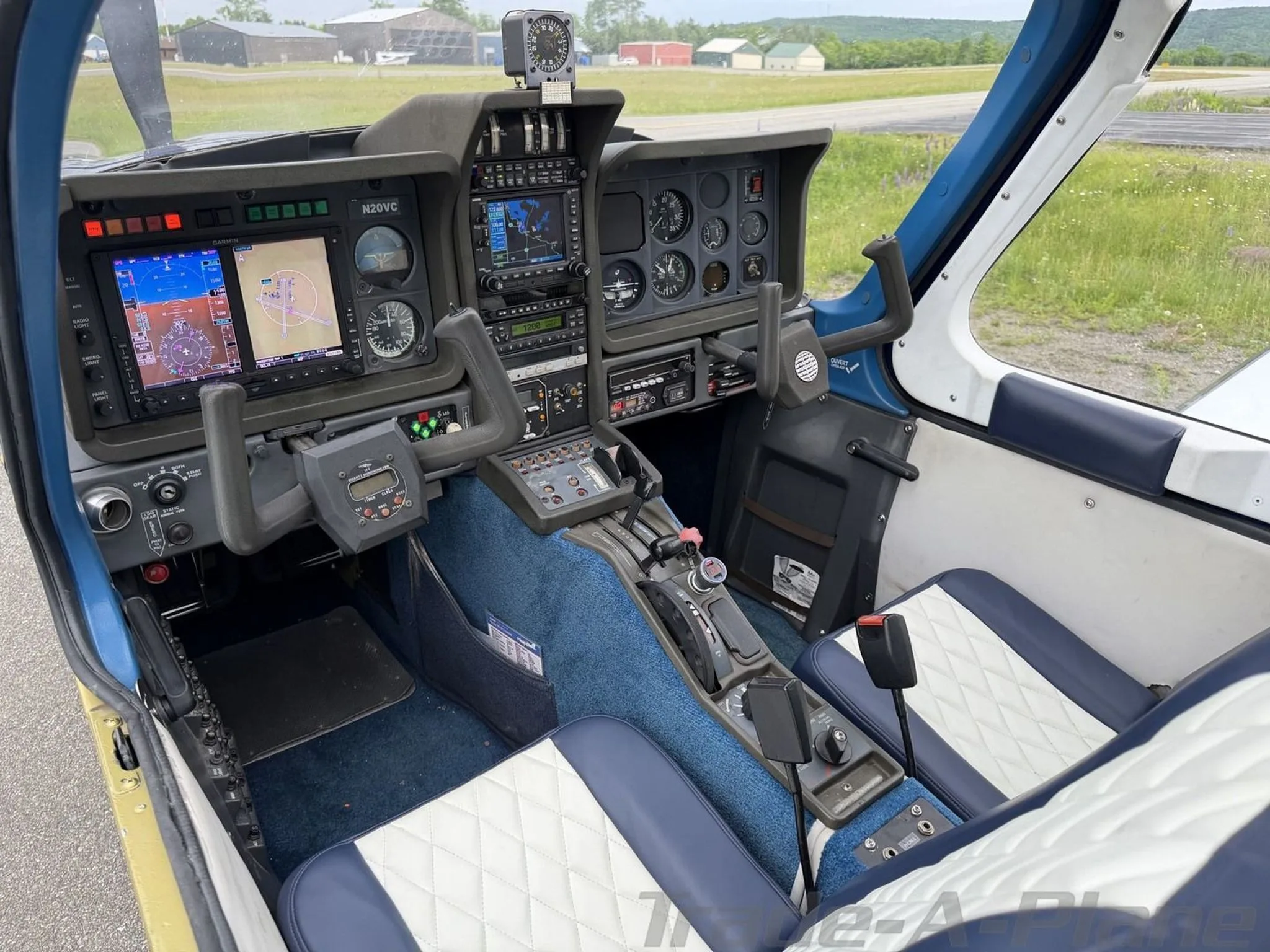 The cockpit of the N20VC aircraft featuring a blue carpet, white and blue quilted seats, and a modern instrument panel with dual screens.