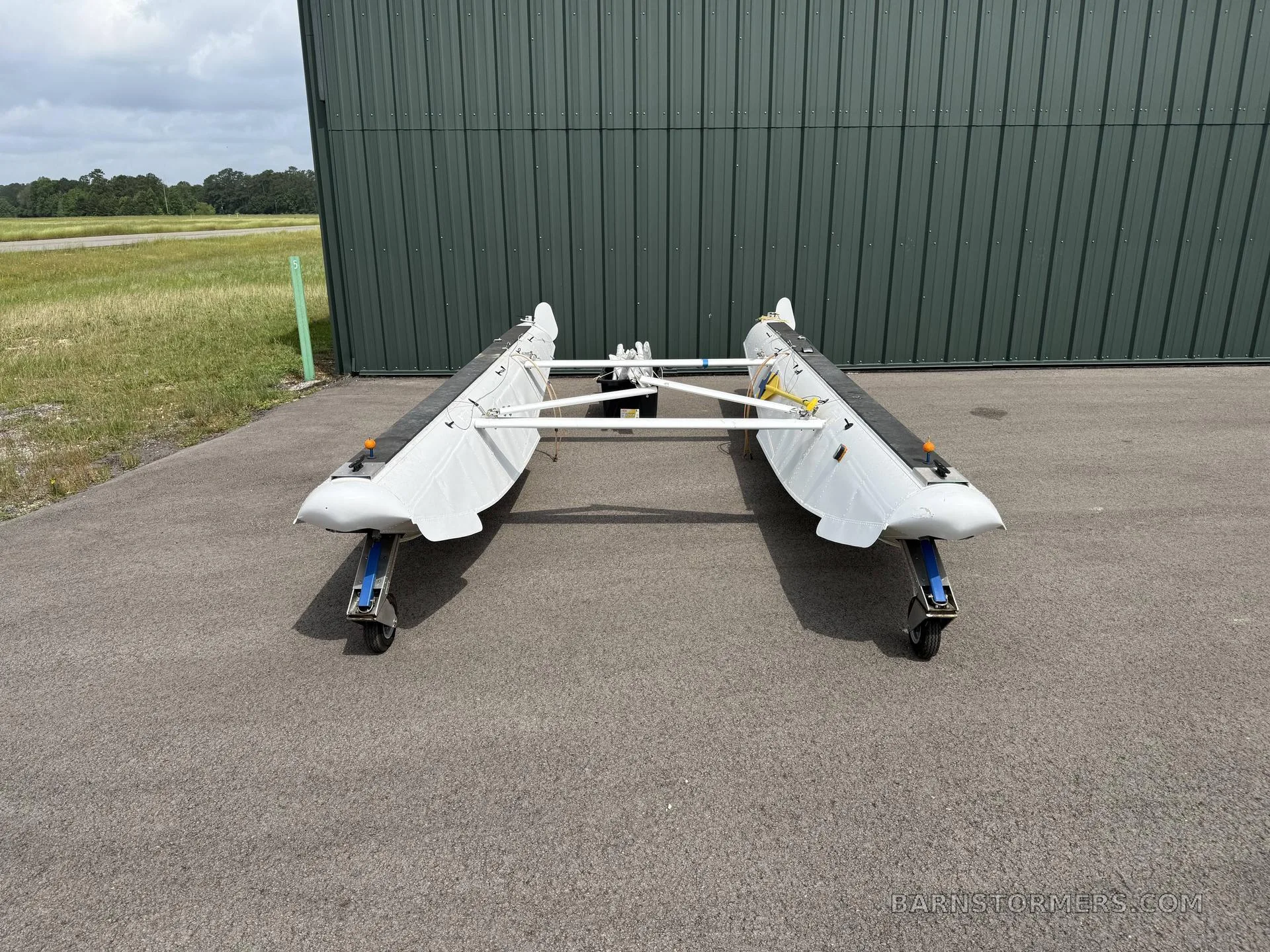 A front view of two white aircraft floats with wheels on an asphalt apron in front of a green hangar.