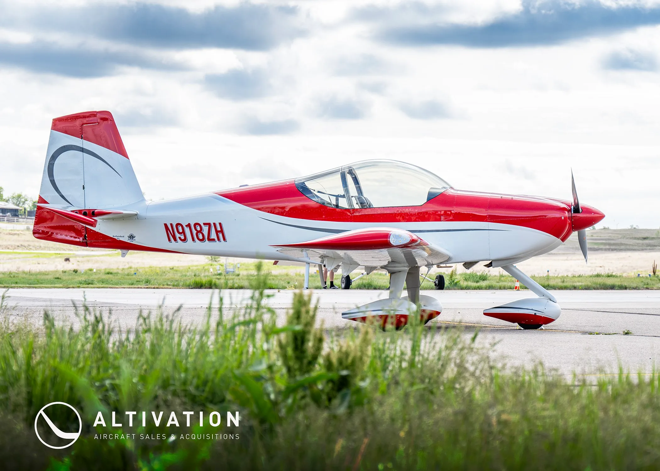 A red and white single-engine aircraft, N918ZH, parked on an asphalt runway with grass in the foreground.