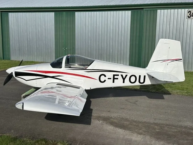 A white single-engine propeller aircraft with red and black stripes, registration C-FYOU, parked on an airfield in front of a hangar.