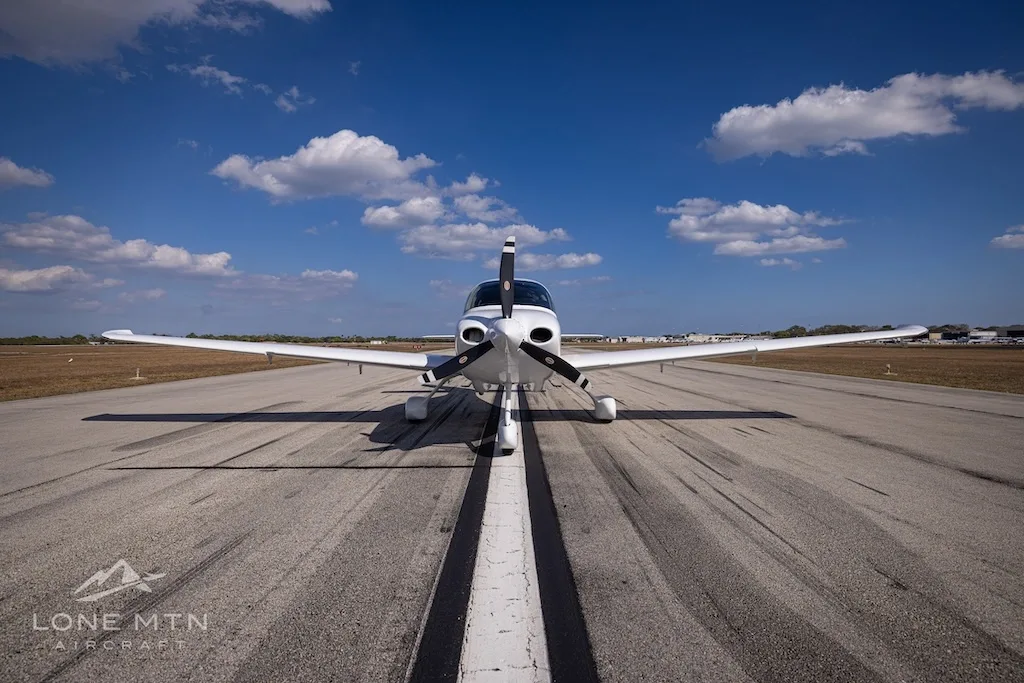 A head-on view of the white N186SB single-engine aircraft with its propeller, centered on a runway.