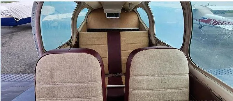 The aircraft's interior cabin with two front seats upholstered in light brown fabric, looking towards the rear seats.