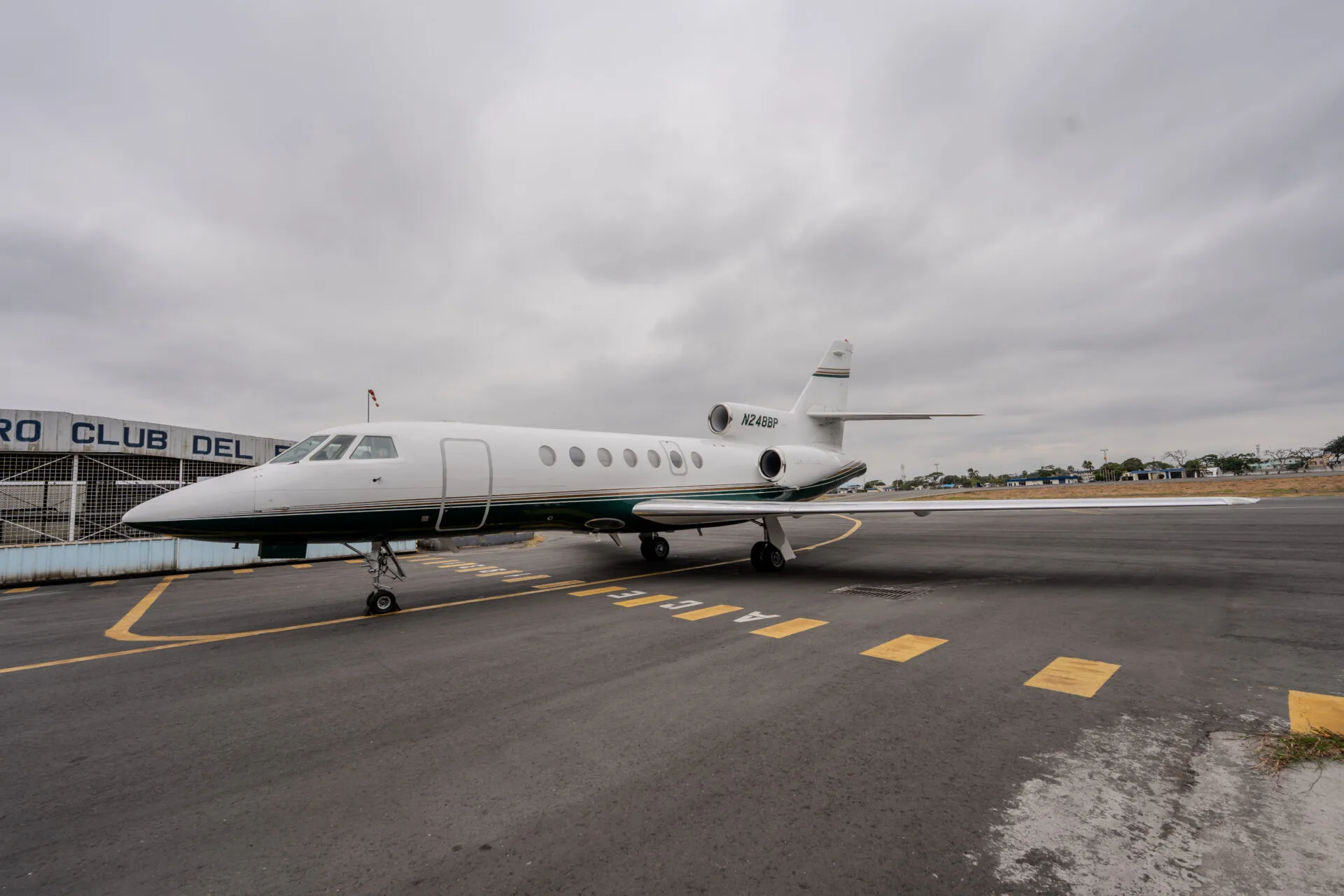 A white and green private jet (N248BP) parked on an airfield under a cloudy sky.