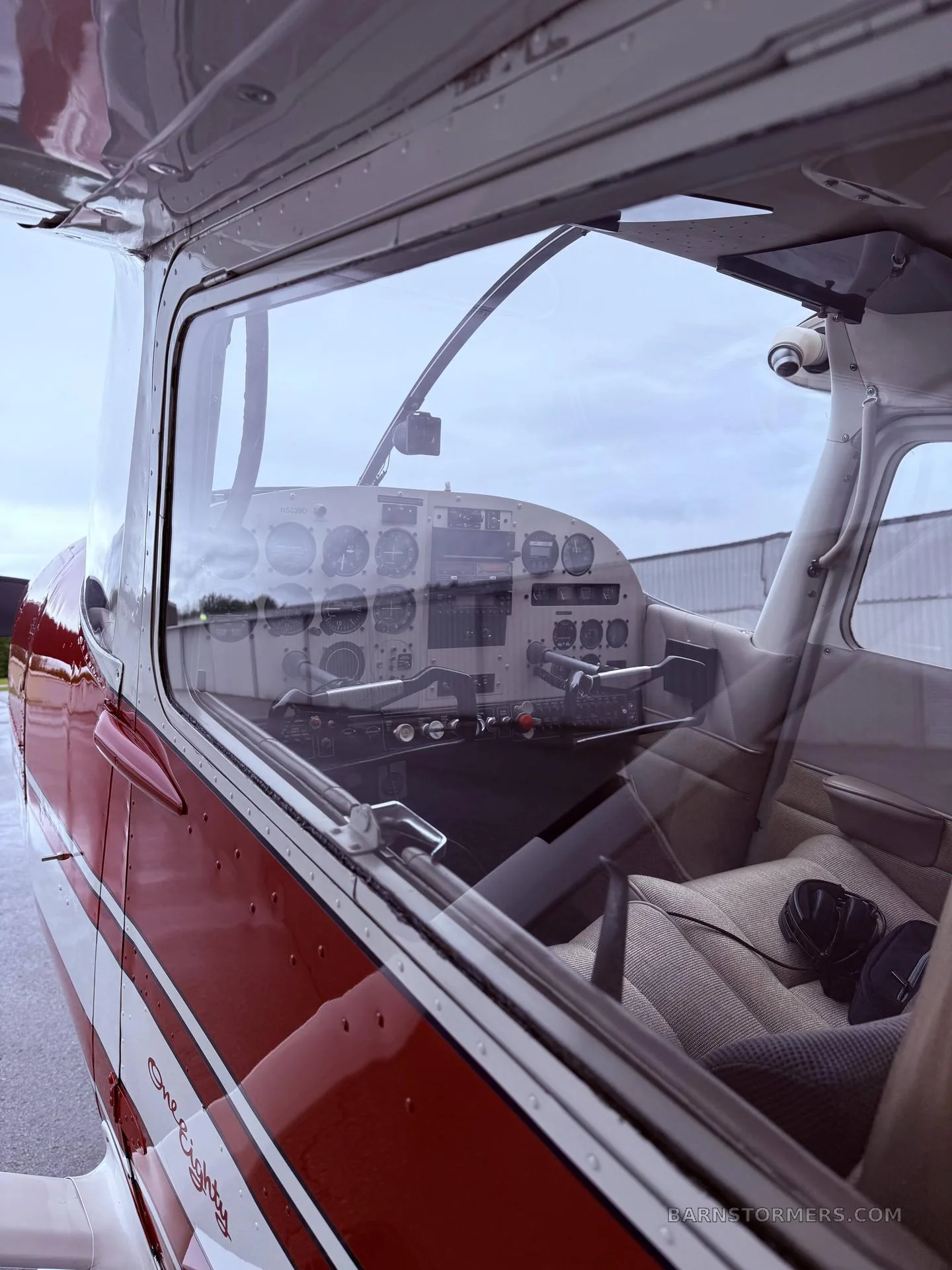 The cockpit of a red and white aircraft is visible through the side window, showing the instrument panel and seats.