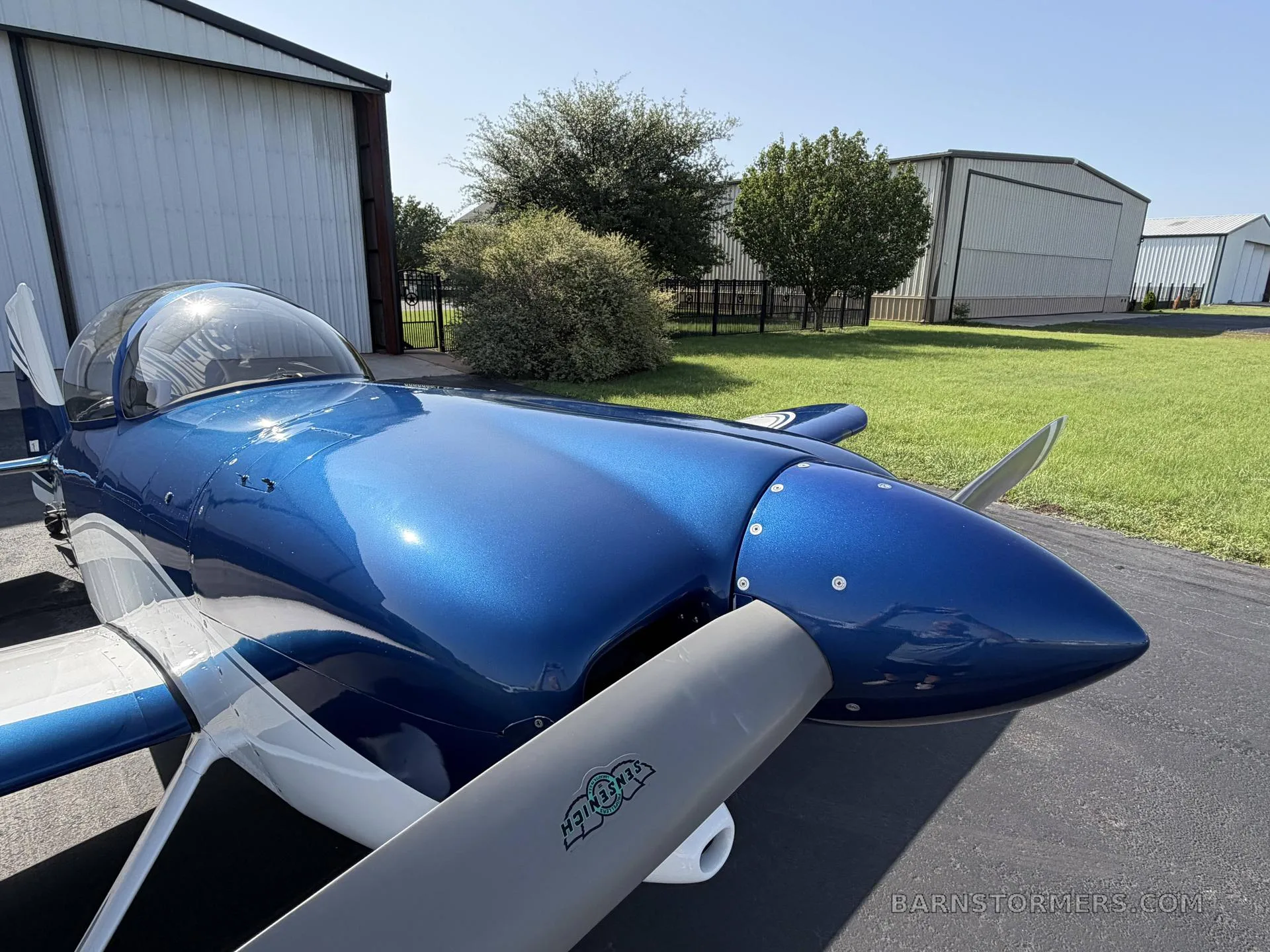 A close-up view of the blue metallic nose and propeller of a single-engine aircraft parked on a tarmac.