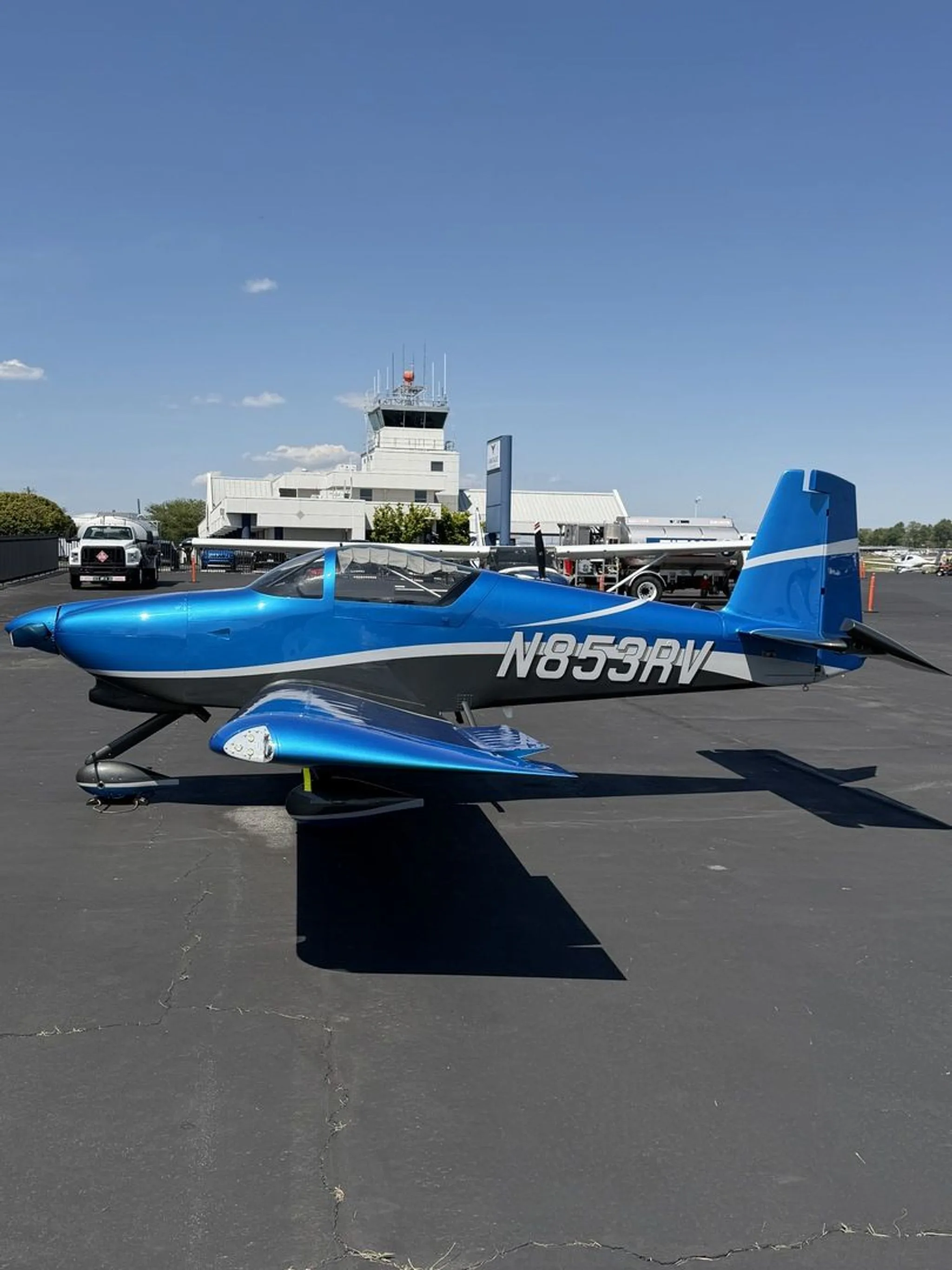 A blue and grey N853RV aircraft parked on an airfield with an air traffic control tower in the background.