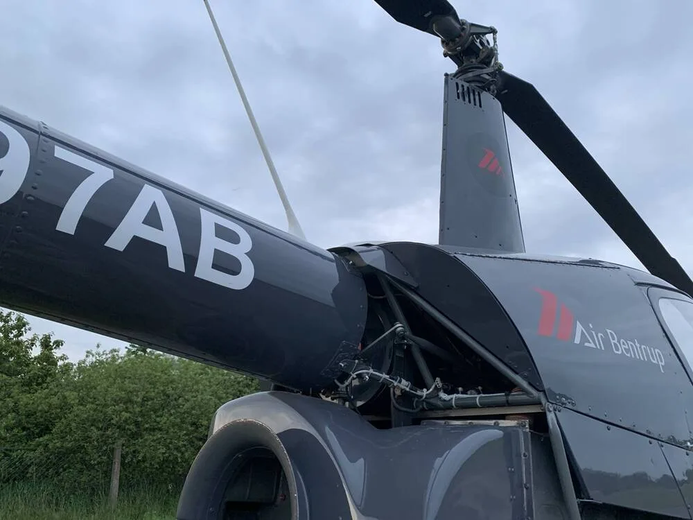 A close-up view of the dark gray fuselage and rotor mast of the Robinson R44 helicopter, N997AB.