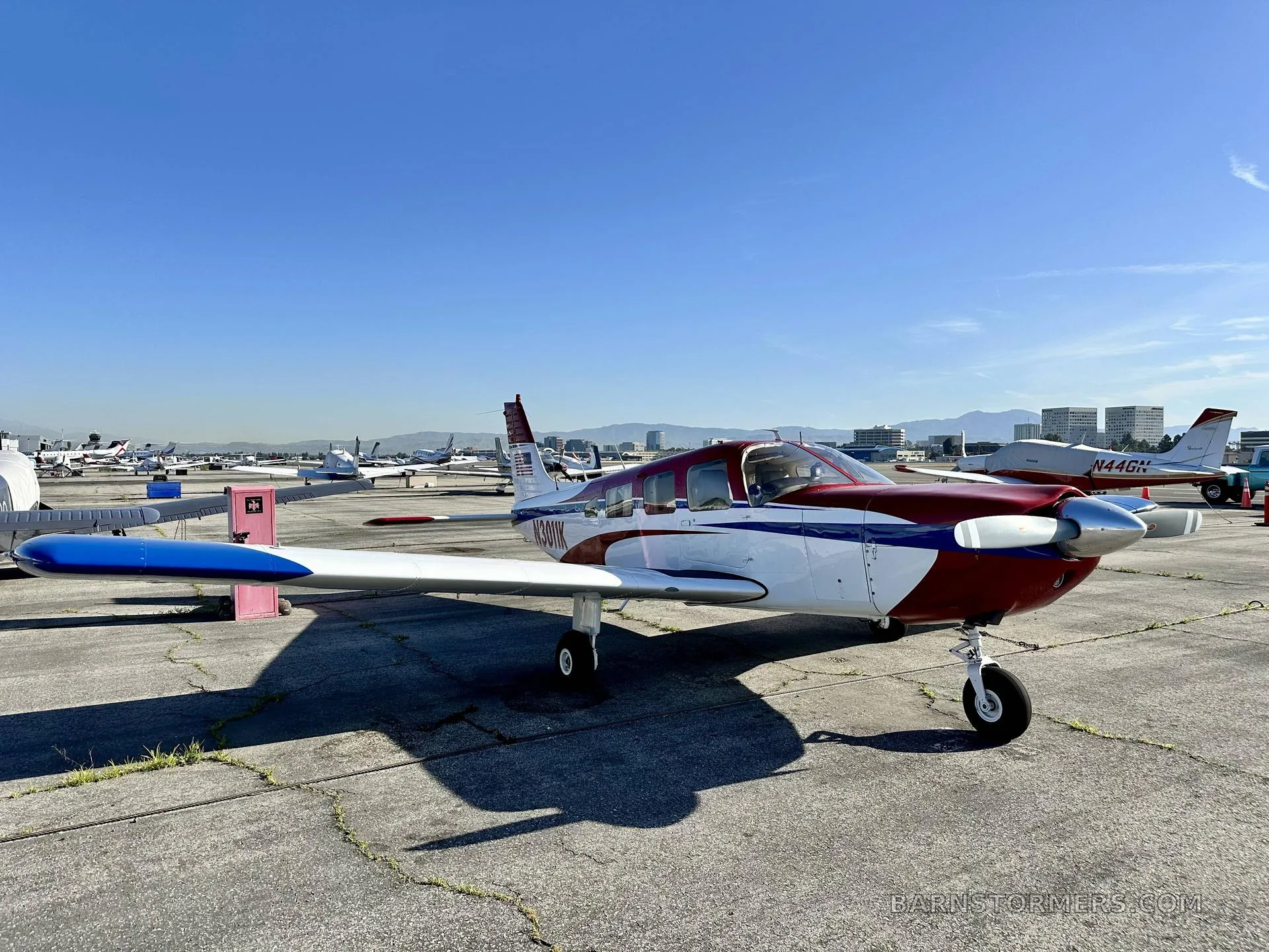 A three-quarter front view of a red, white, and blue single-engine propeller aircraft (N3011K) on an airport ramp.