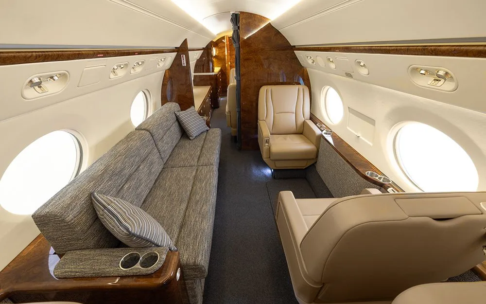 A section of the private jet cabin interior with a long sofa and a single beige leather seat.