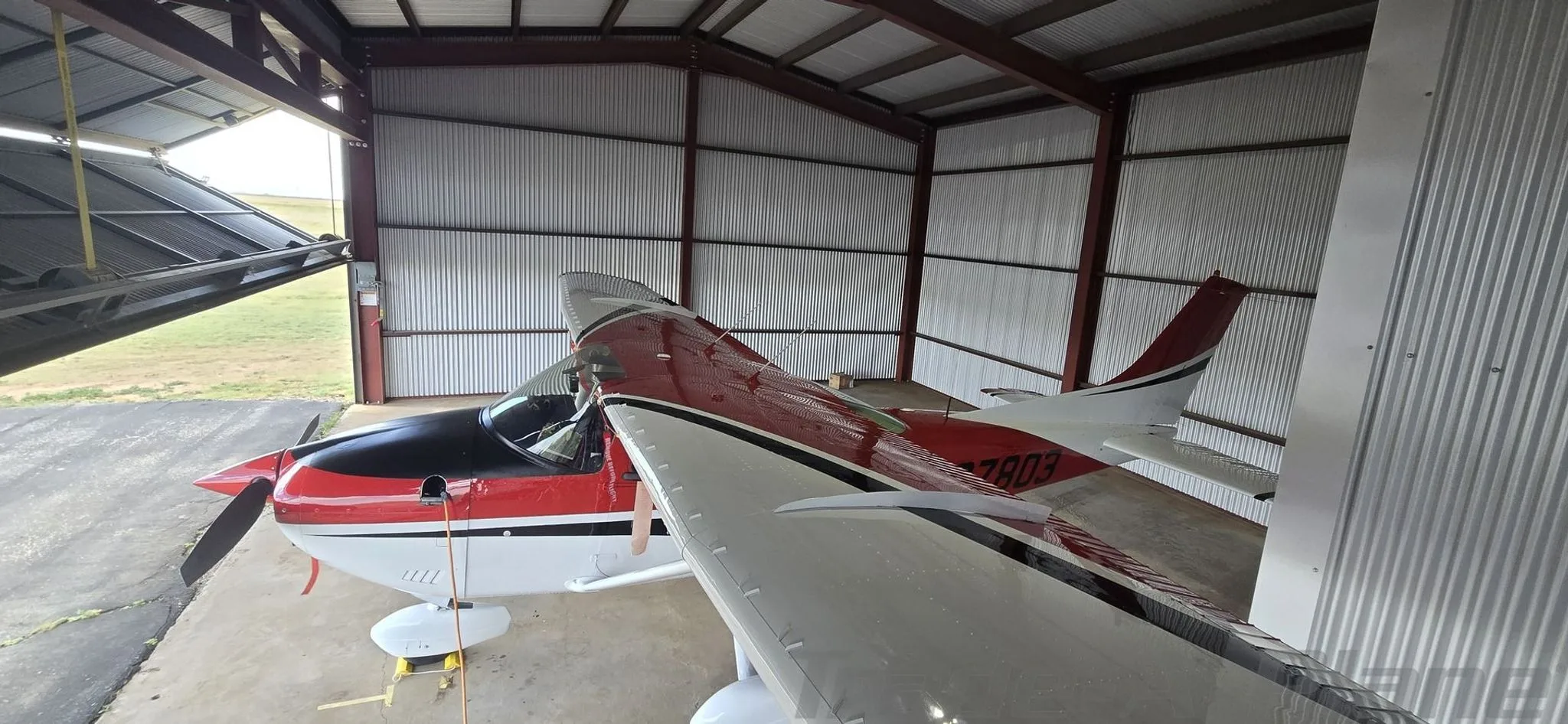 A red, white, and black Cessna aircraft (N97803) is parked inside a metal hangar.