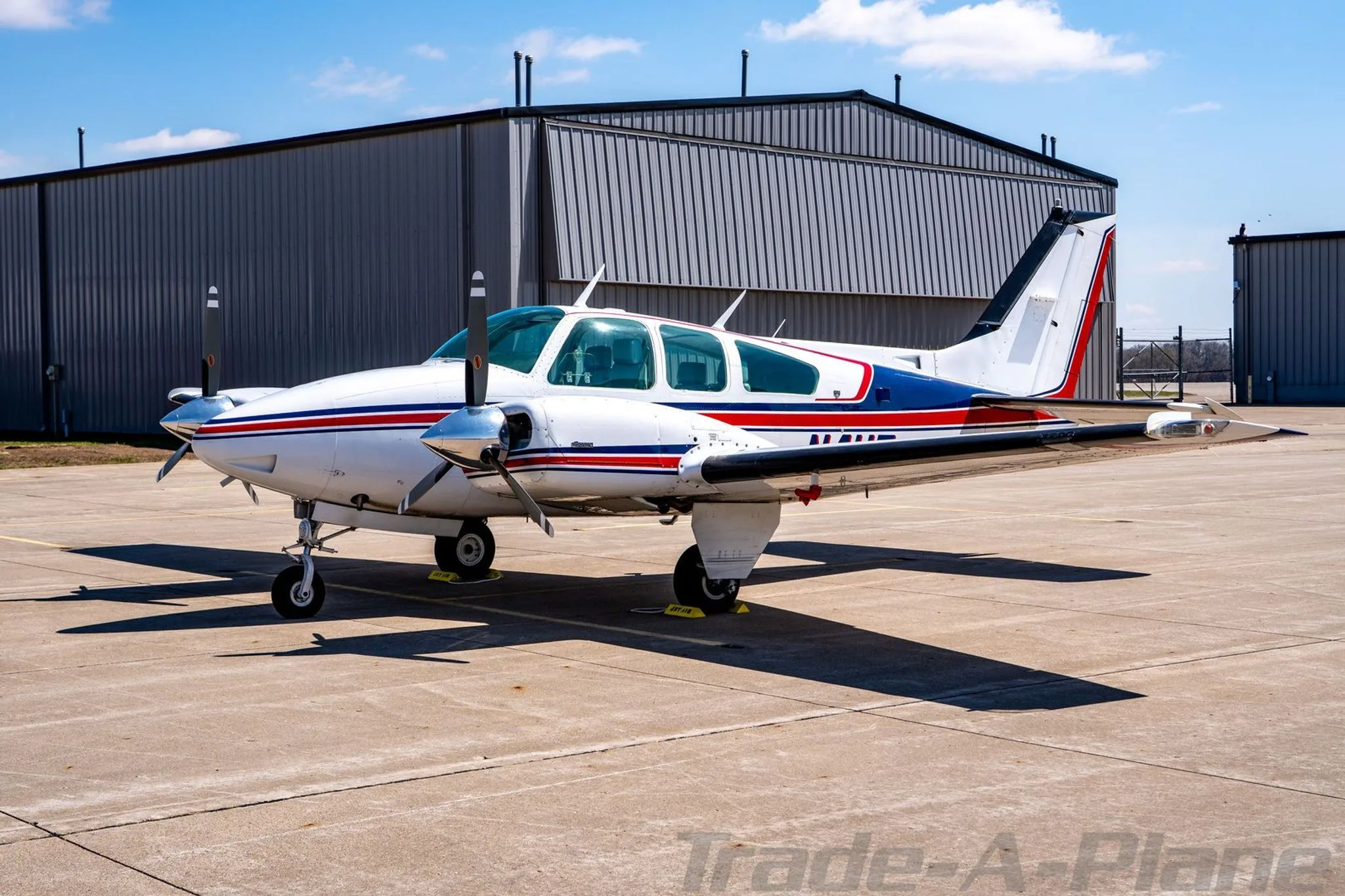 Side view of the N4UF twin-engine Beechcraft Baron with red and blue stripes parked on an airfield.