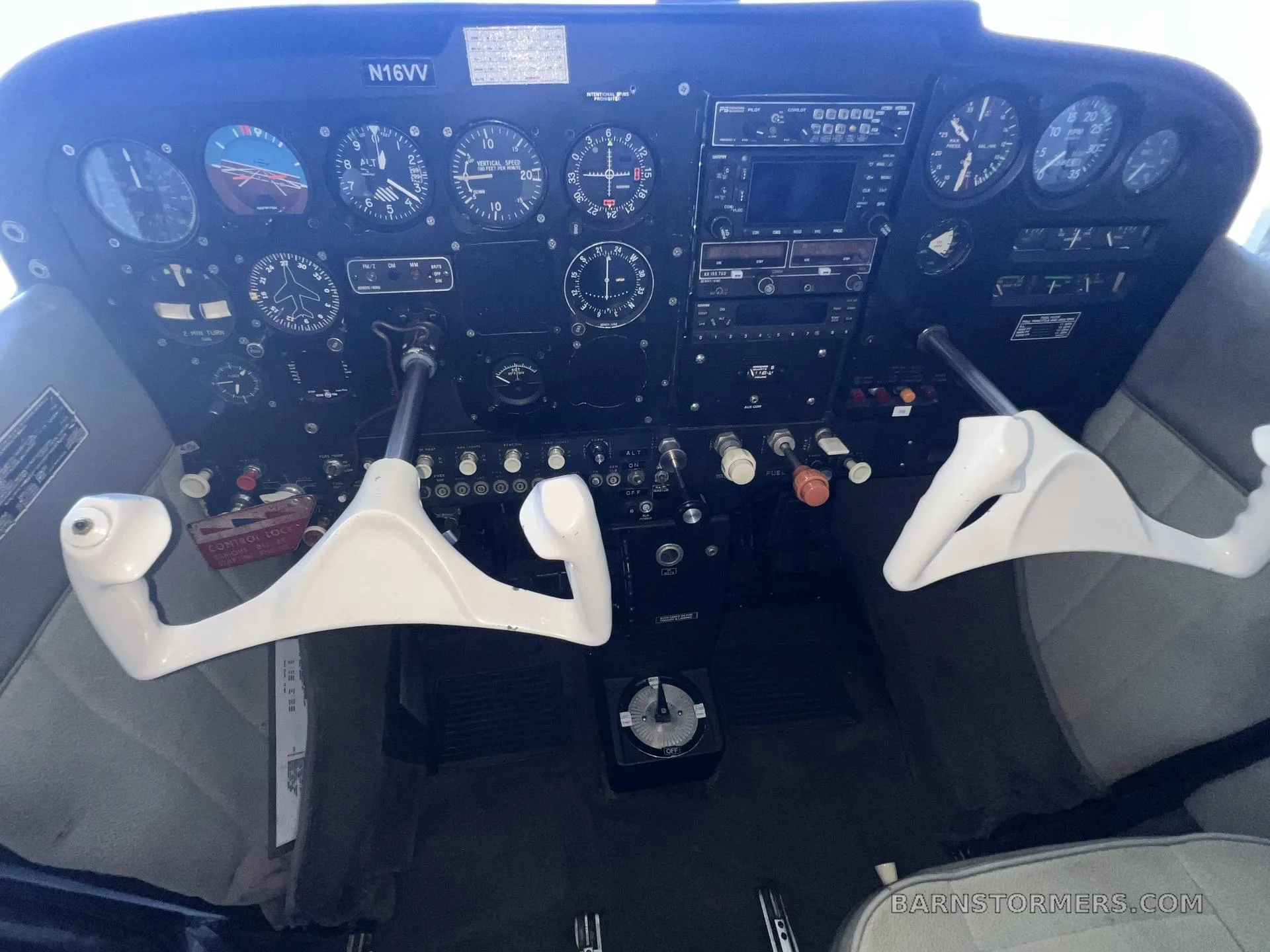 The cockpit of an aircraft featuring a detailed instrument panel with various gauges, radios, and white control yokes.
