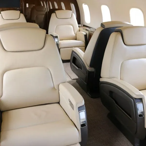 Close-up view of two beige leather aircraft seats in a private jet cabin.