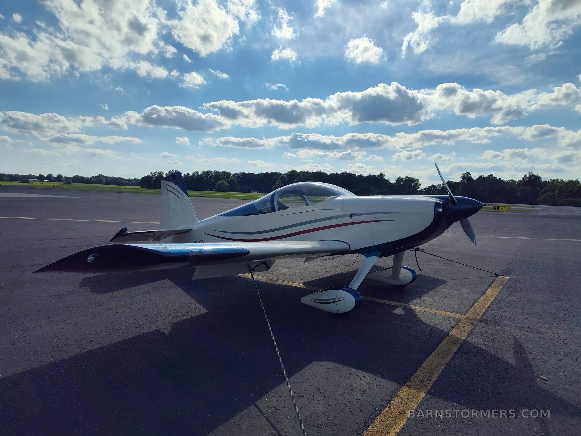 A cream and blue single-engine aircraft with red and grey stripes, viewed from the front-left, parked on an asphalt tarmac.