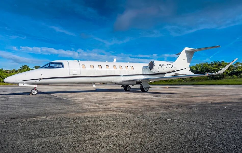 A white business jet with registration PP-FTX is parked on an asphalt runway under a blue sky with scattered clouds.