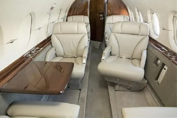 The luxurious cabin interior of a private jet with light-colored leather seats and a wooden fold-out table.