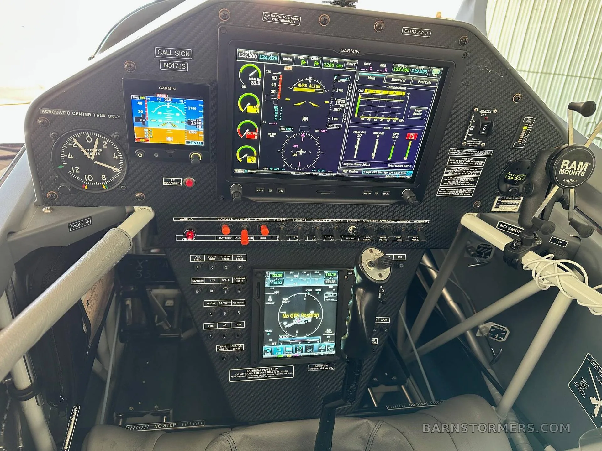 The cockpit of an Extra 300LT aircraft features a modern glass panel with Garmin displays and a carbon fiber finish.
