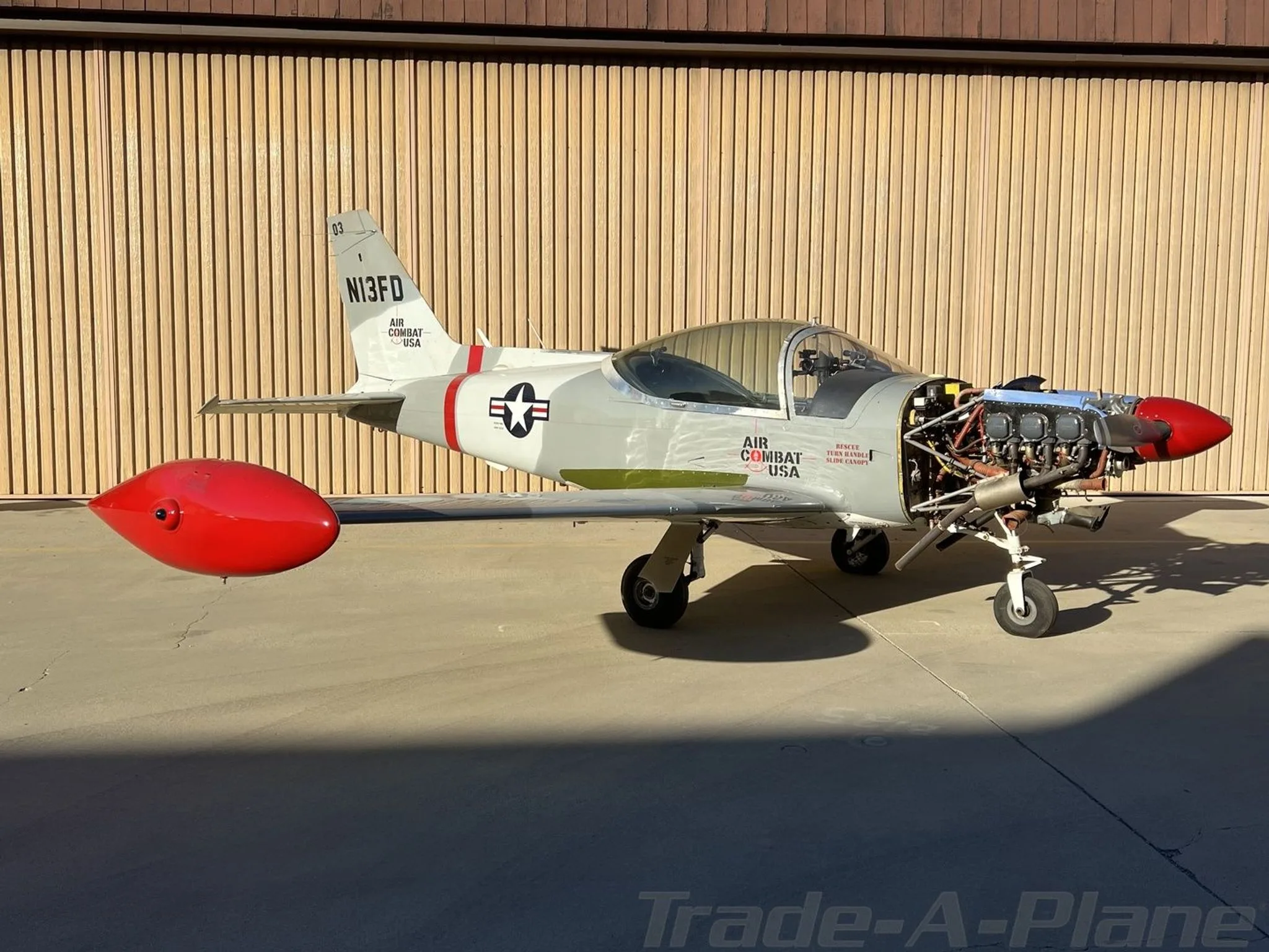 A side view of the N13FD aircraft parked on the tarmac, with its engine exposed and a red wingtip tank.