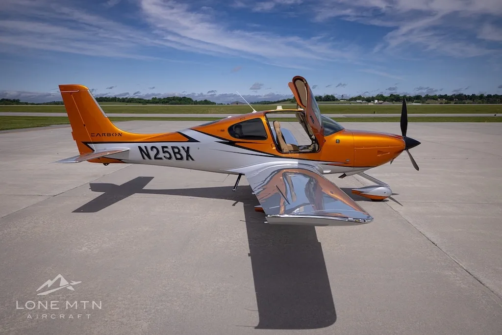 A side-right view of the orange and silver Cirrus SR22T N25BX with its doors open on an airfield.
