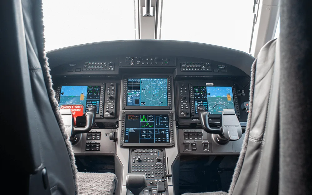 The modern glass cockpit of a Pilatus PC-12 aircraft, featuring multiple large display screens and control yokes.