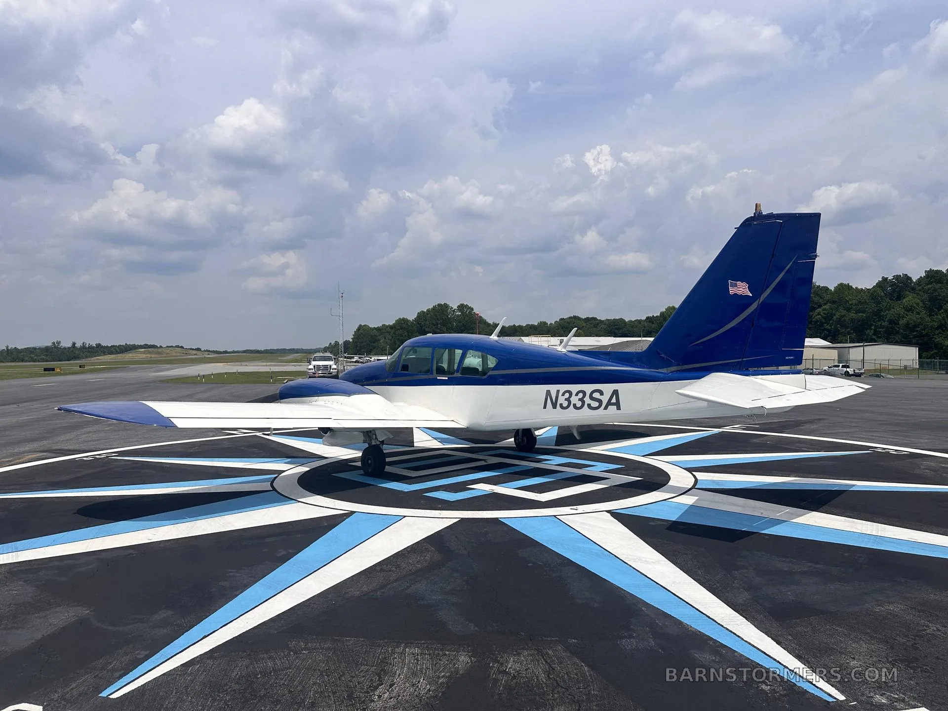 A three-quarter rear view of a blue and white single-engine aircraft (N33SA) parked on a compass rose marking on an airfield.