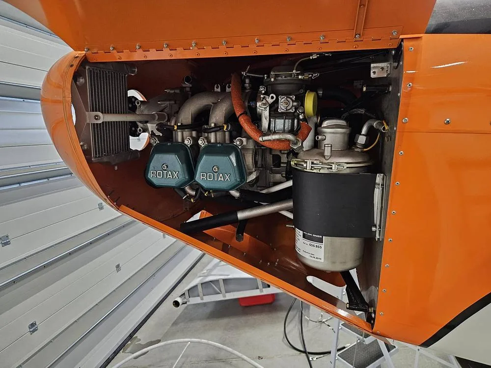 A close-up view of the Rotax engine installed in the orange aircraft, with its cowling open.