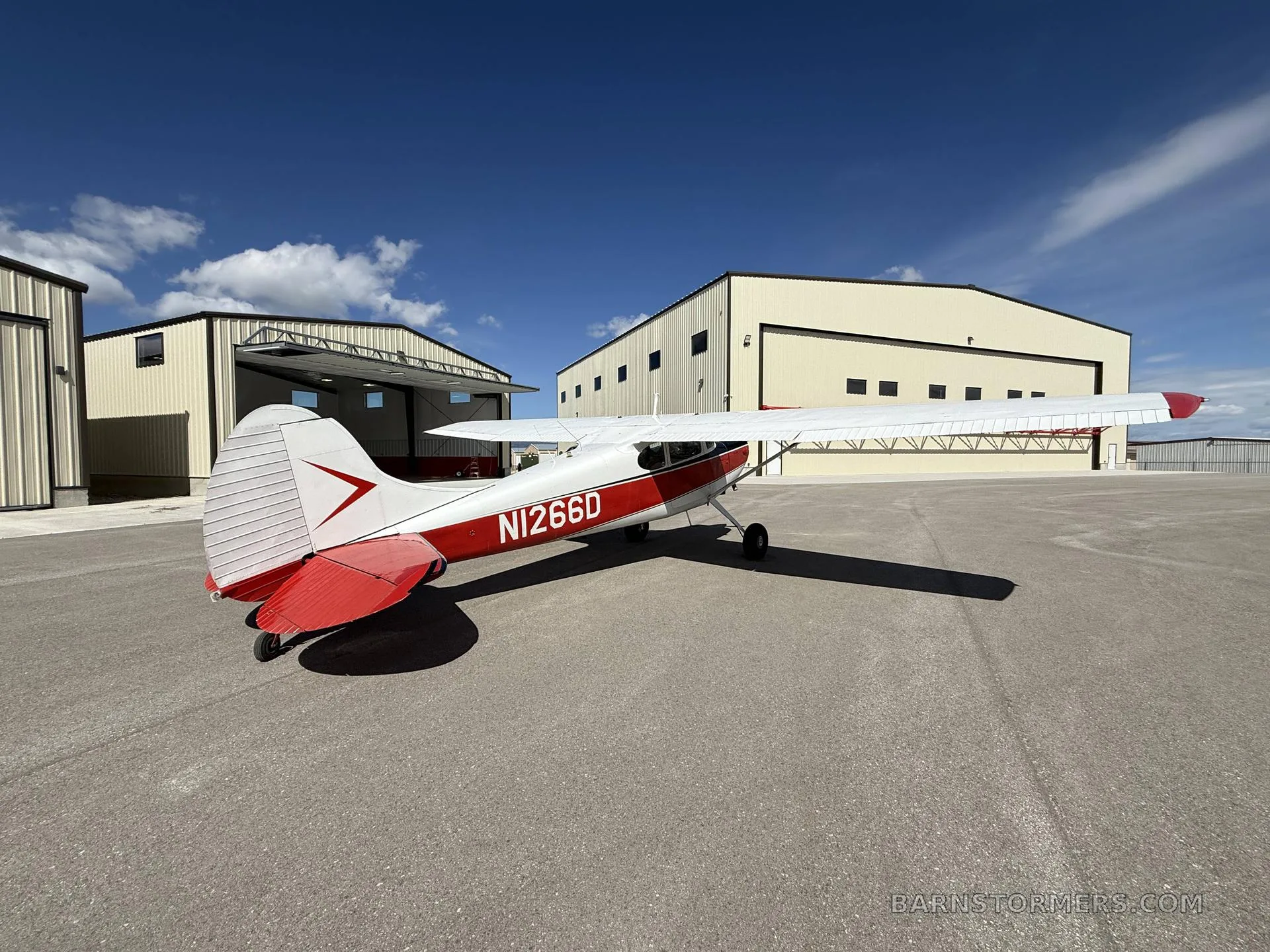 A red and white Cessna 170B (N1266D) is parked on an airfield, viewed from the rear-right, showing the tail and wing.