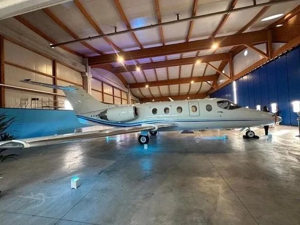 A sleek white business jet with blue accent stripes parked inside a modern hangar with wooden beams.