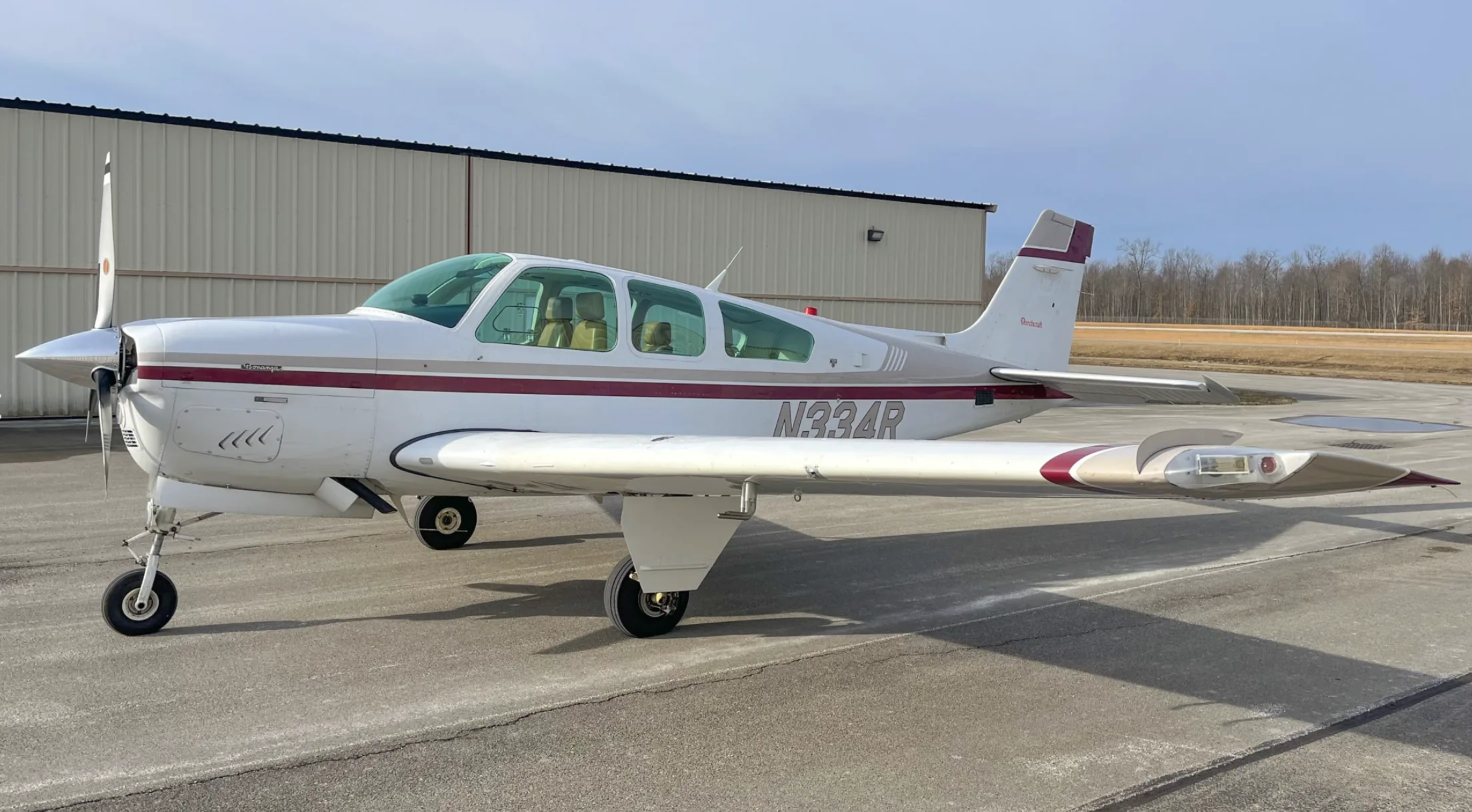 A side view of a white and maroon Beechcraft Bonanza aircraft, tail number N334R, parked on a tarmac.