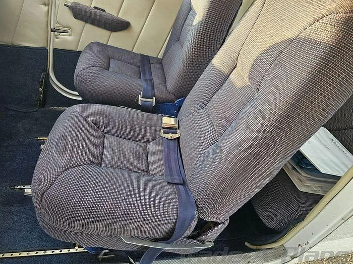 The interior cabin of a Cessna 182 Skylane, showing two rows of blue patterned fabric seats with seatbelts.