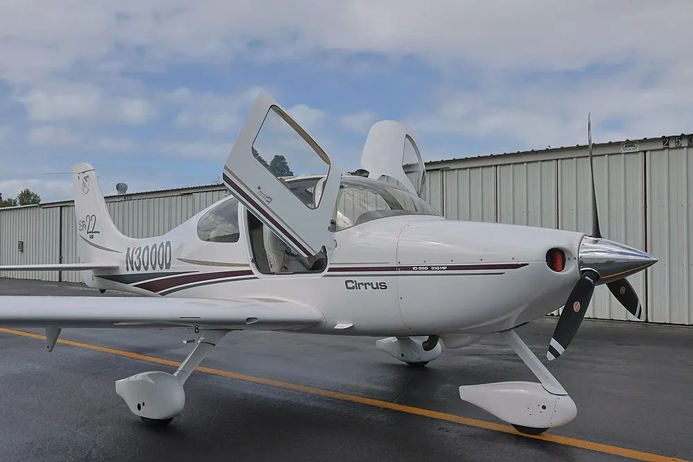 Front-right view of a white Cirrus SR22 aircraft with N3000D registration and both doors open, parked on a wet tarmac.