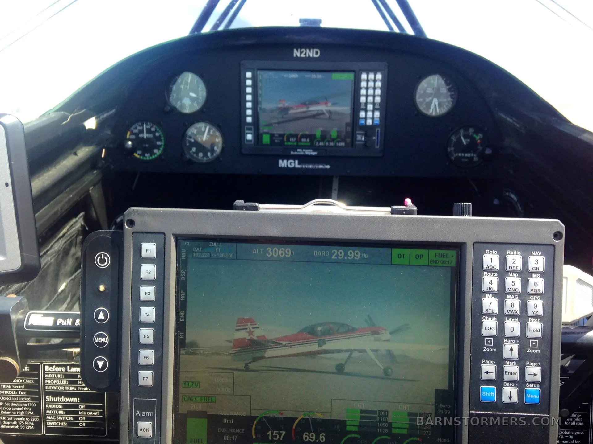 The interior of an aircraft cockpit, featuring multiple MGL Avionics displays, one showing a red and white biplane on an airfield.