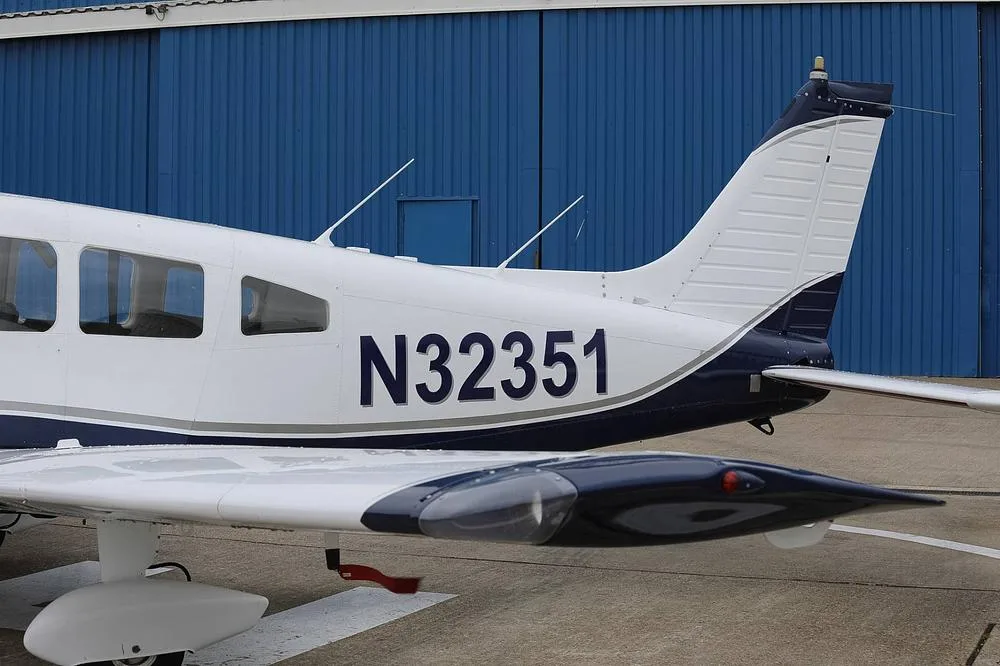 A close-up view of the tail and wing of a white and blue Piper PA-28 aircraft showing registration N32351.