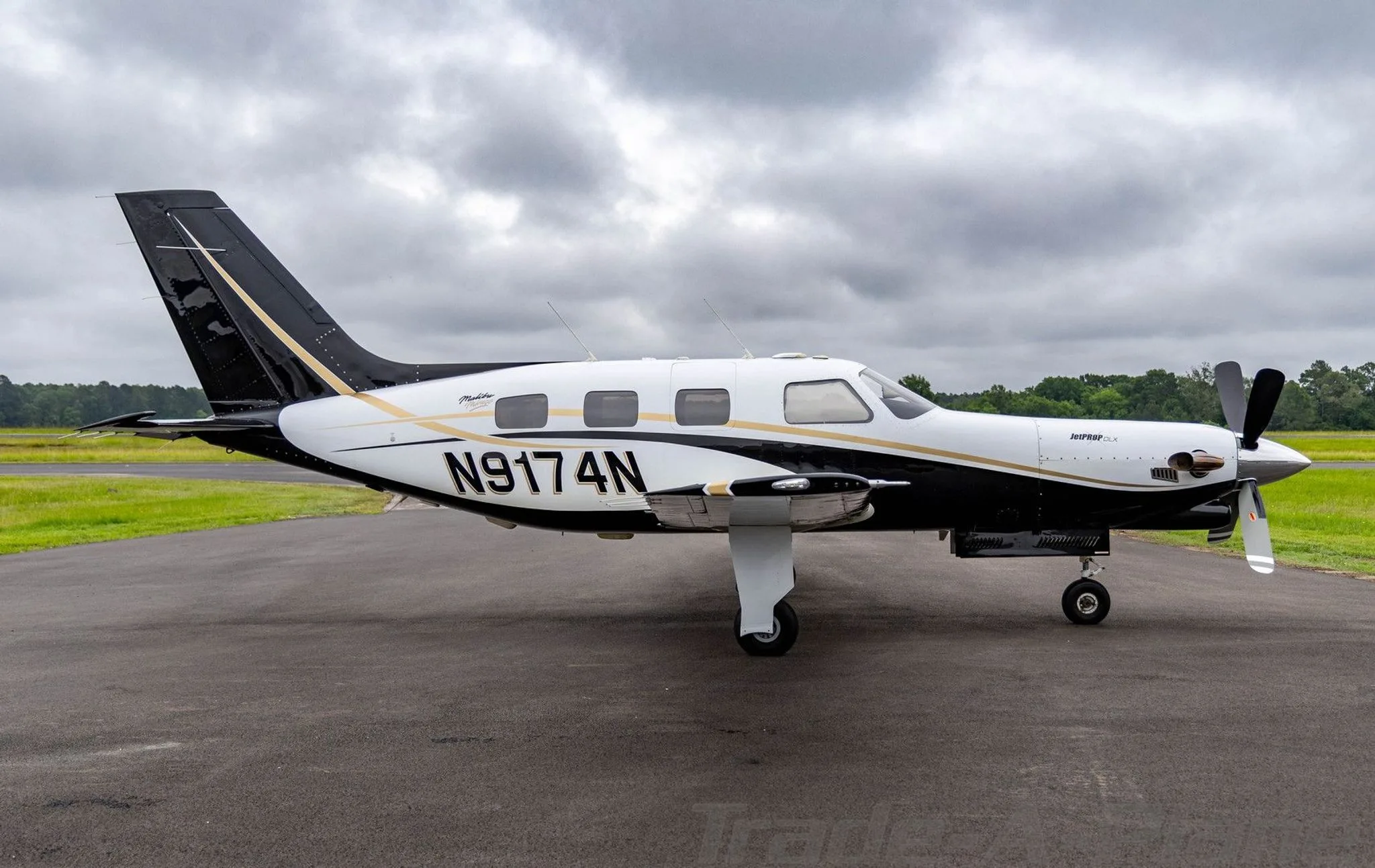 A white and black Piper Malibu Mirage (JetPROP DLX) N9174N with gold accents parked on a tarmac, viewed from the right side.