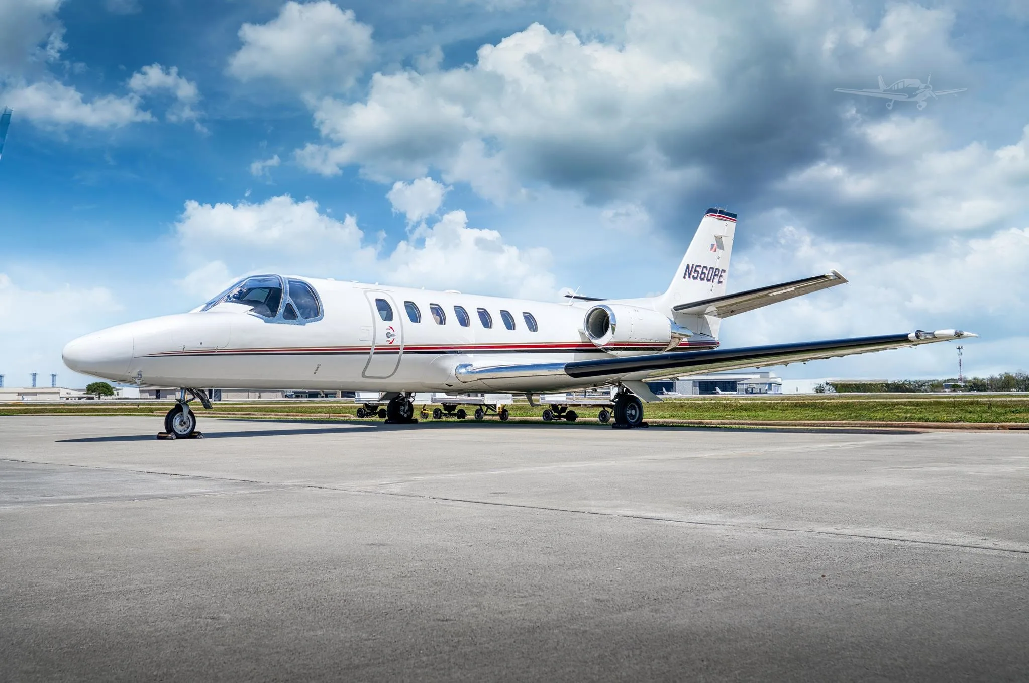 A white Cessna Citation V (N560PE) private jet is parked on an airport tarmac under a partly cloudy sky.
