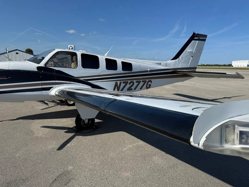 A close-up view shows the tail and wing of the white and black twin-engine aircraft, N7277G, on an airfield.