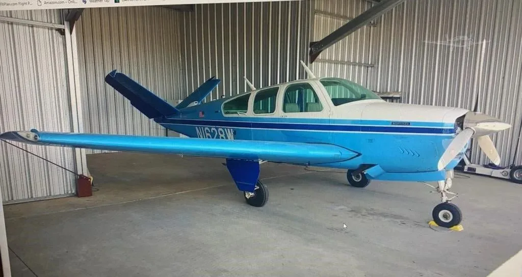 A blue and white Beechcraft Bonanza aircraft, registration N1628W, parked inside a hangar.