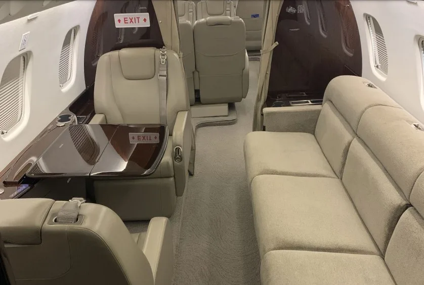 The luxurious cabin interior of an aircraft, featuring beige leather seats, a polished wooden table, and a comfortable sofa.