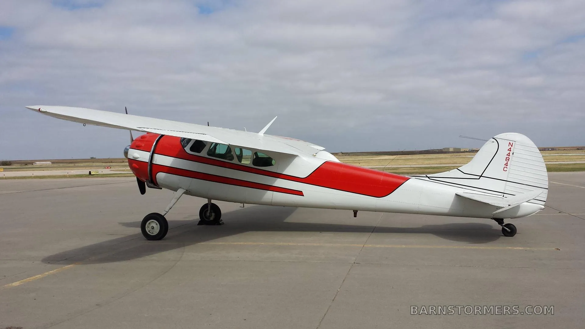 A side view of a red and white single-engine propeller aircraft with registration N484C parked on an asphalt runway.